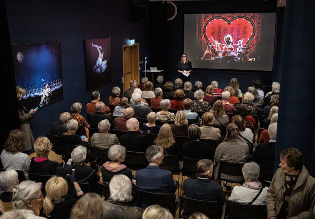 Mennesker i en sal ser på bildet på en skjerm