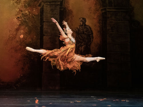 Ballerina i gyllen kjole gjør splitthopp
