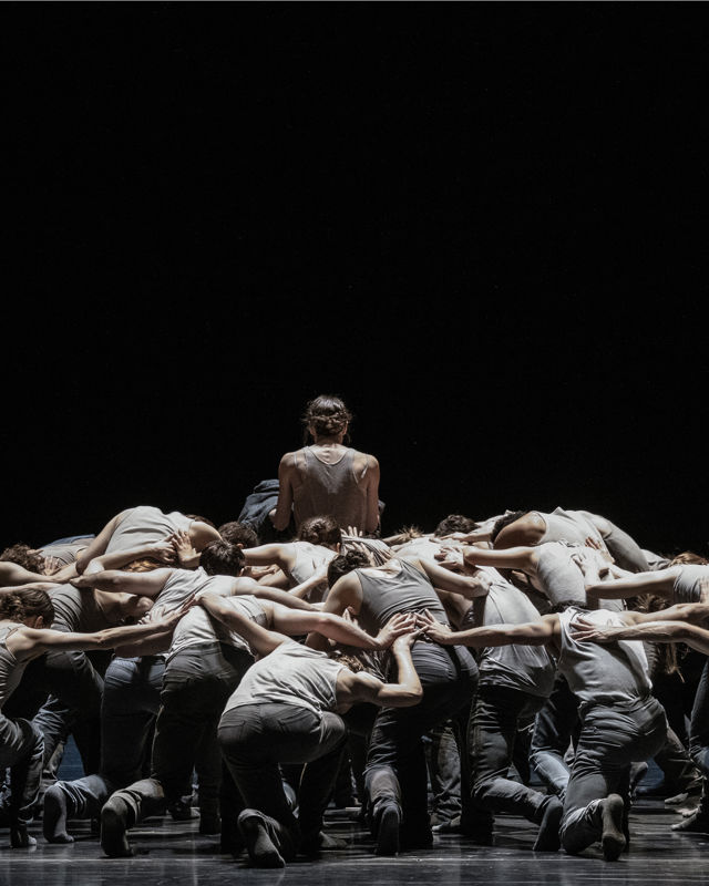 en gruppe dansere bøyer seg mot scenegulvet, en danser står i midten med  ryggen til