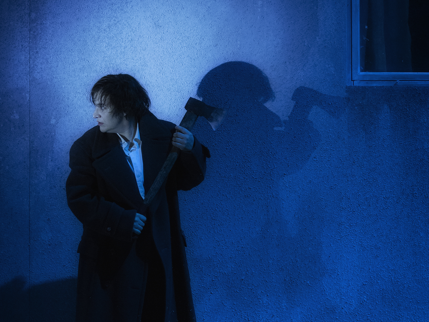 Kvinne med øks i blått lys foran hus