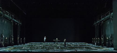 tre dansere midt på en mørk scene md blågrønt opprørt hav under seg