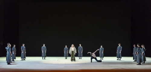 en stor gruppe dansere kledd i grå kapper samlet på scenen