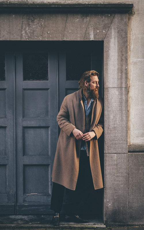 Mann i brun frakk foran døråpning