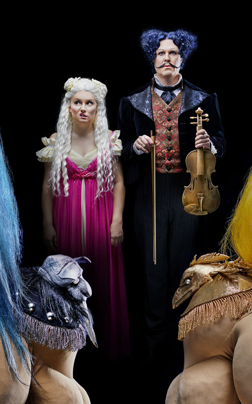 Fantasilignende figurer med blå og gule parykker, foran en kvinne og en ann med fiolin i bakgrunnen