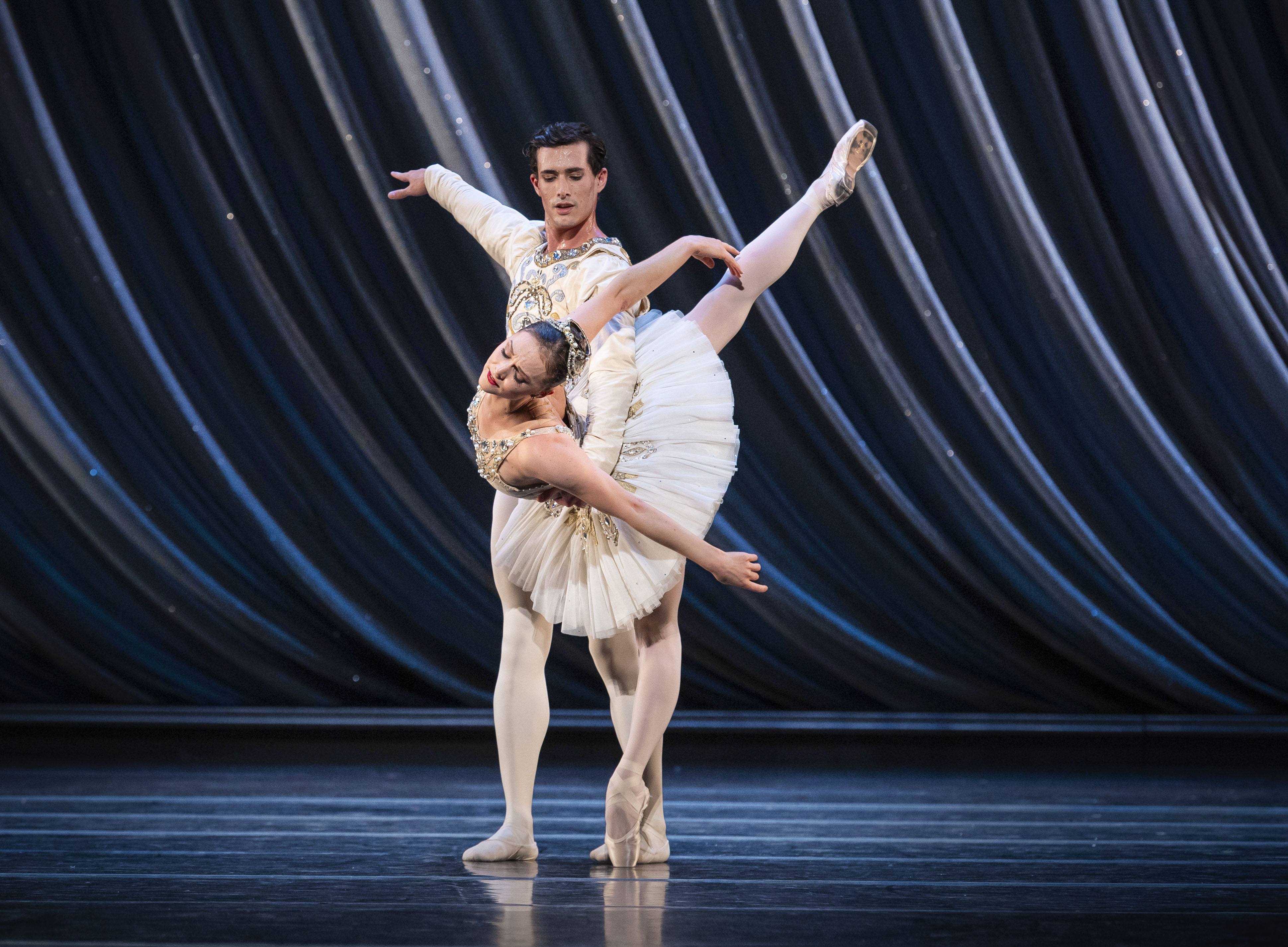 en mann i hvitt holder en kvinnelig danser i hvit tutu og tåspissko