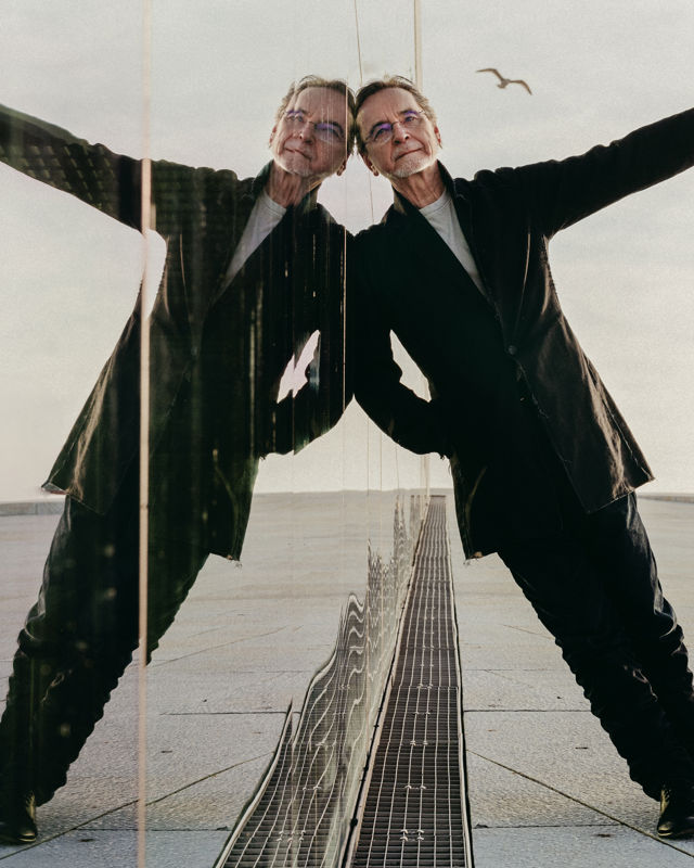 en mann lener seg mot glass som speiler han. en måke flyr i bakgrunnen