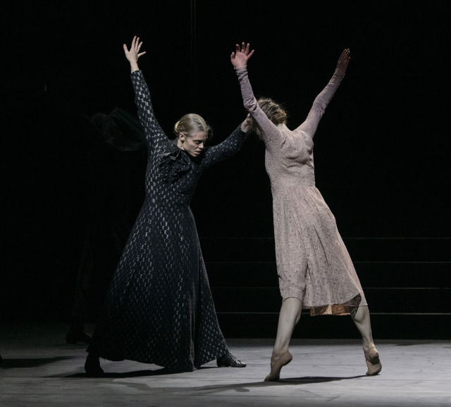 To dansere møter hverandre i en løftet, dramatisk bevegelse på mørklagt scene.