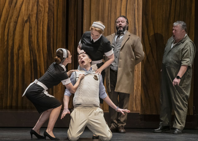 Redd mann sitter på kne på gulvet, to damer og to menn rundt ham