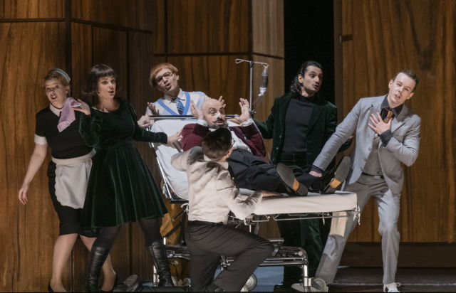 Mann ligger på sykeseng med flere stående rundt