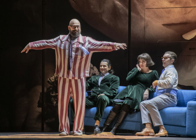 Mann i rødstripete pysjamas, tre andre sitter på sofa i bakgrunnen