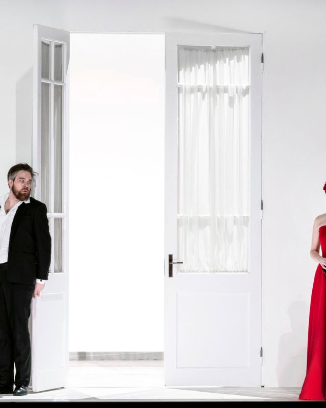 To menn i dress, delvis bak dør, ser på kvinne i lang, rød kjole