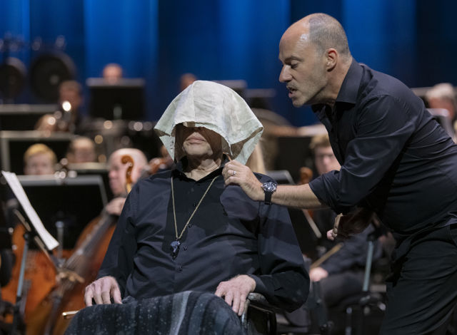 Mann legger lommetørkle over en mann som sitter foran et orkester