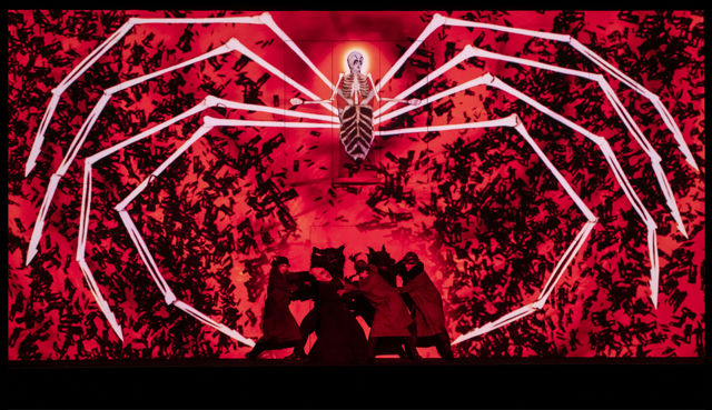 Stor animert hvit edderkopp mot rød bakgrunn, noen slåss på gulvet nedenfor