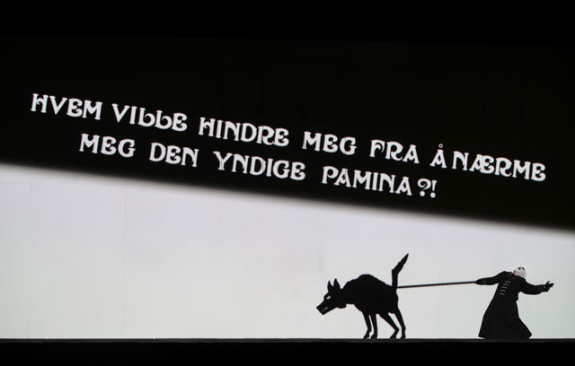 Scenebilde med mann som holder animert hund i halsbånd, med tekstplakat på veggen over.