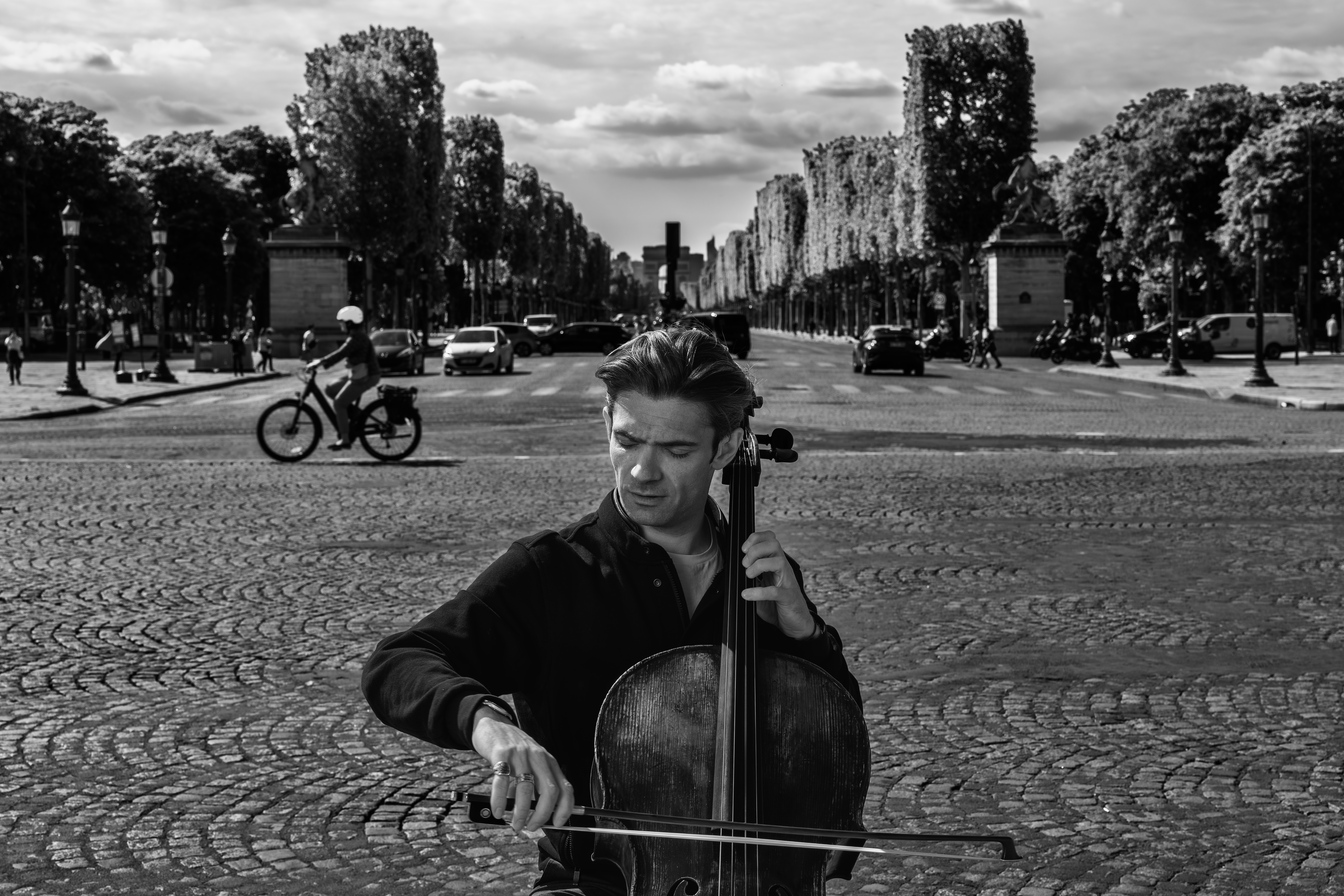 Svarthvitt portrett av cellisten Gautier Capucon med cello på en brostenslagt plass
