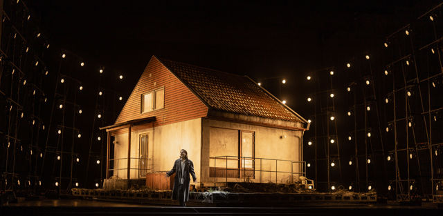 Kvinne står foran hus på en scene med lyskastere rundt på alle kanter